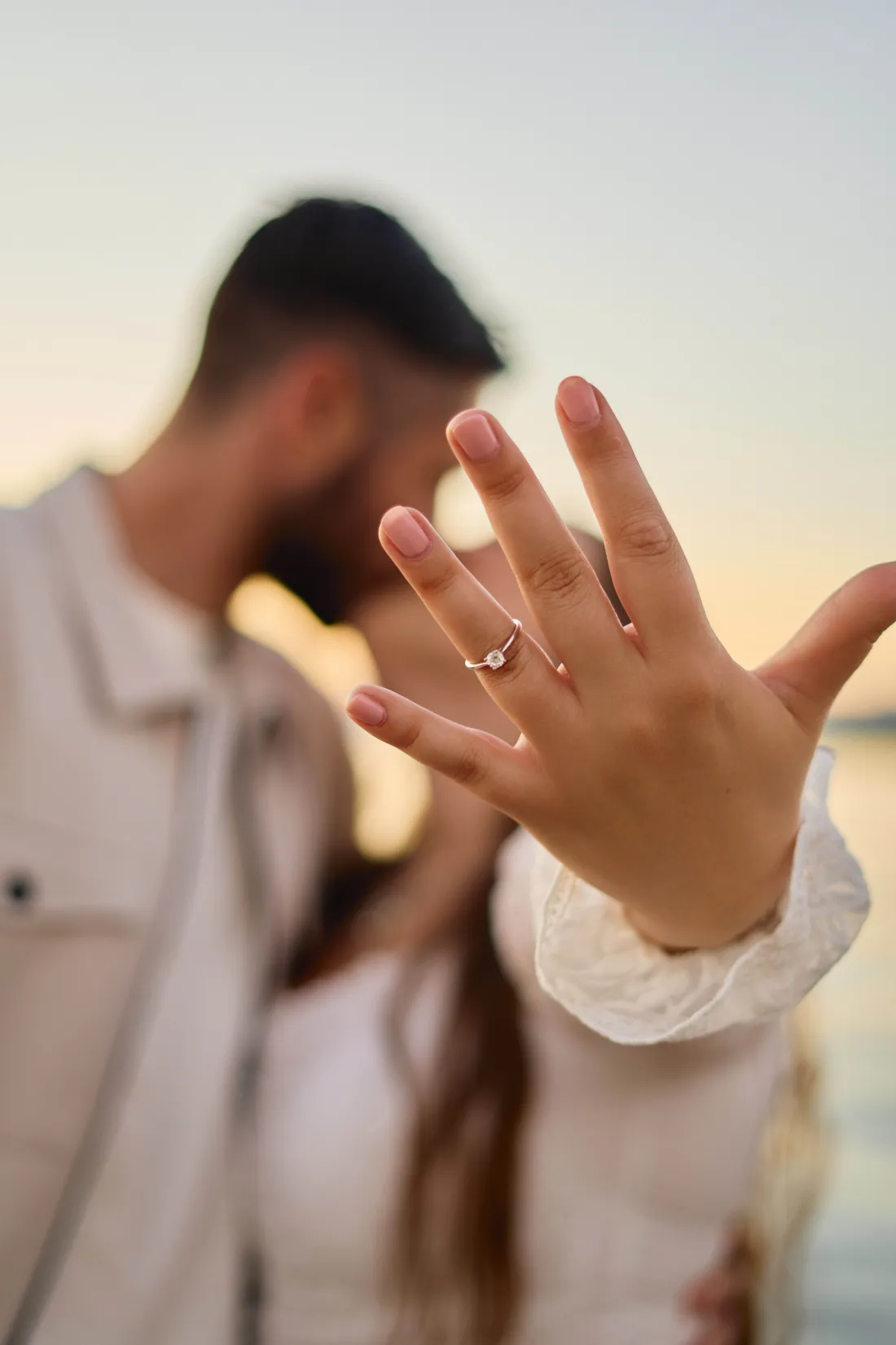 Engagement ring close-up as the couple kiss behind her hand