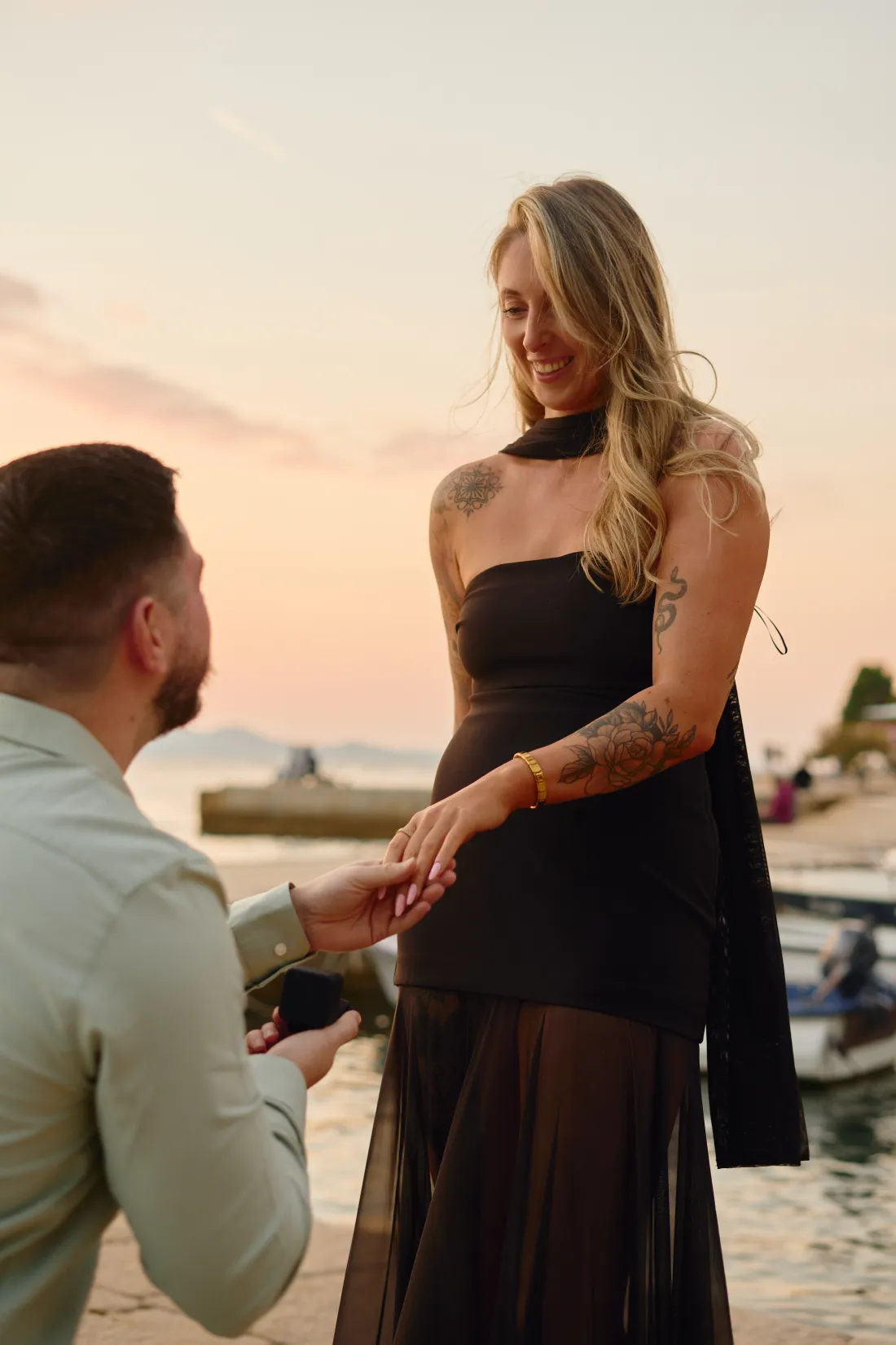 Man on one knee at a white floral heart arch during a proposal by the sea