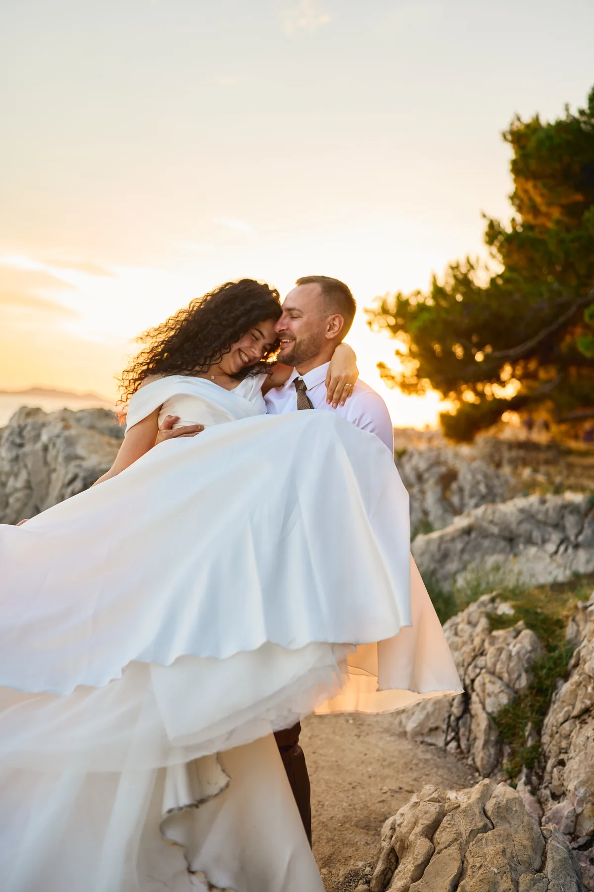 Groom lifting his bride at golden hour on the rocky coast