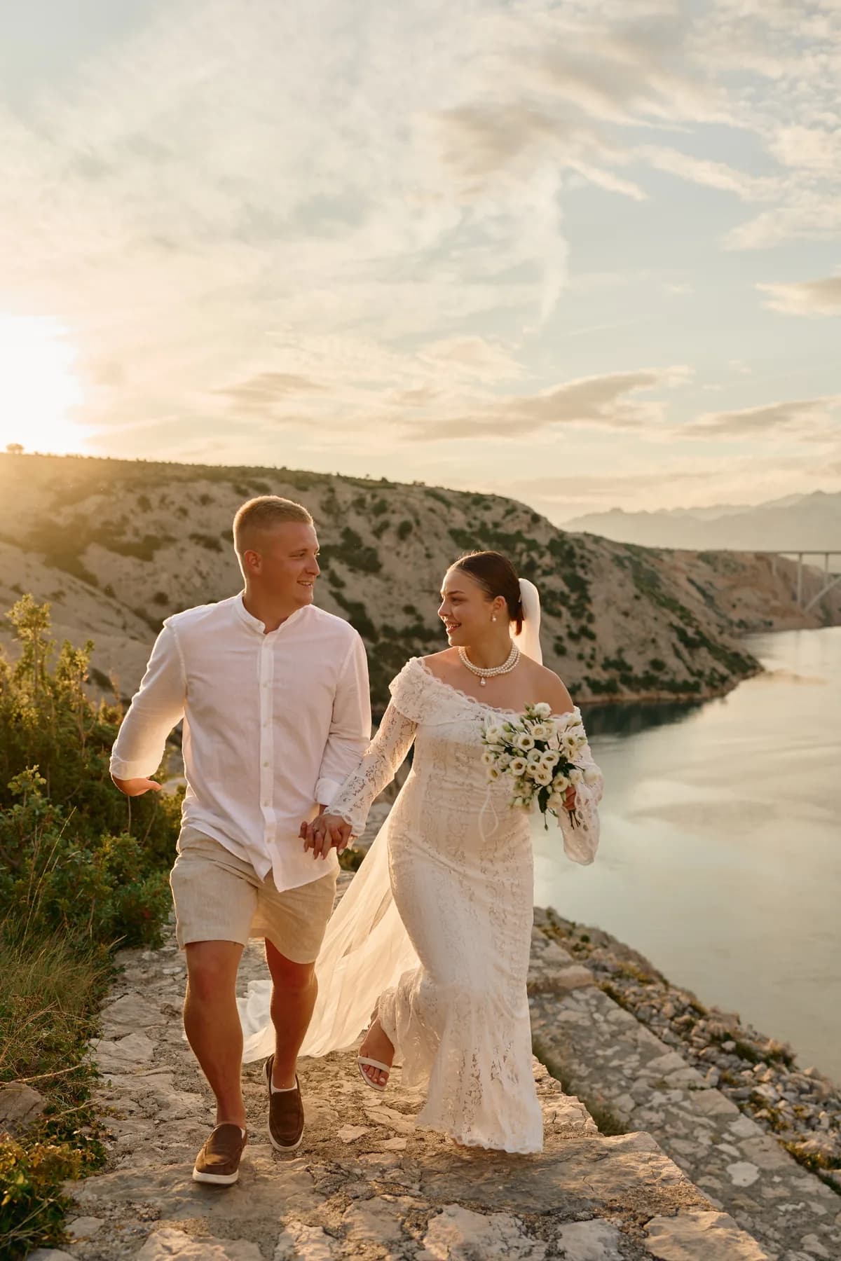 Couple walking down the rocks above the sea at sunset