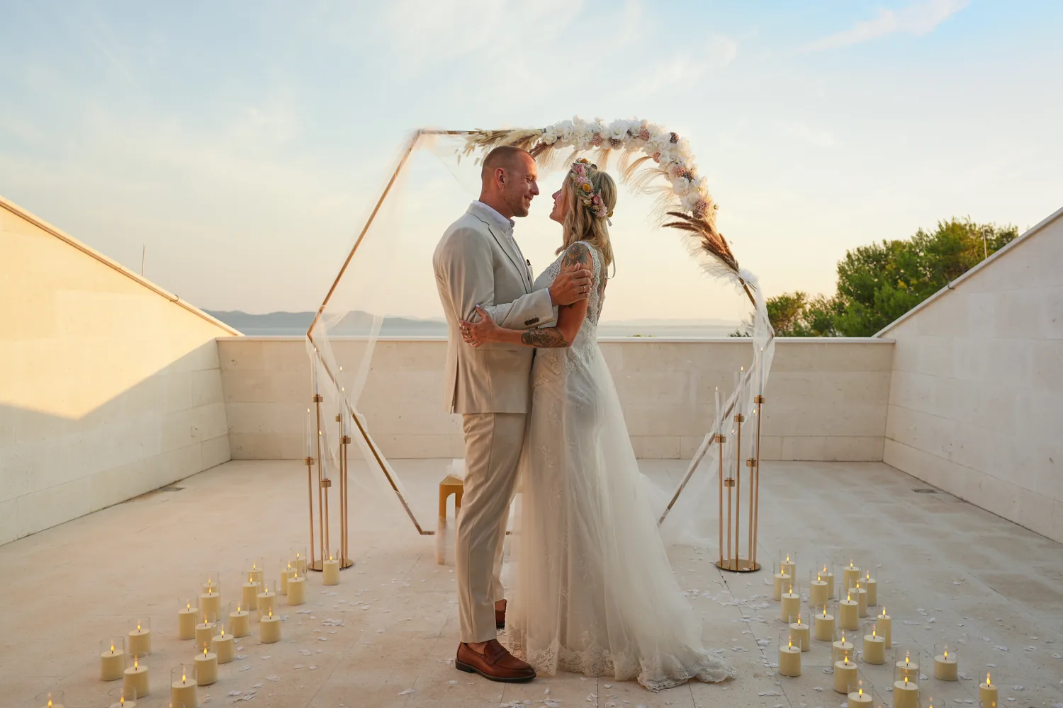 Bride and groom under a floral ceremony arch at sunset