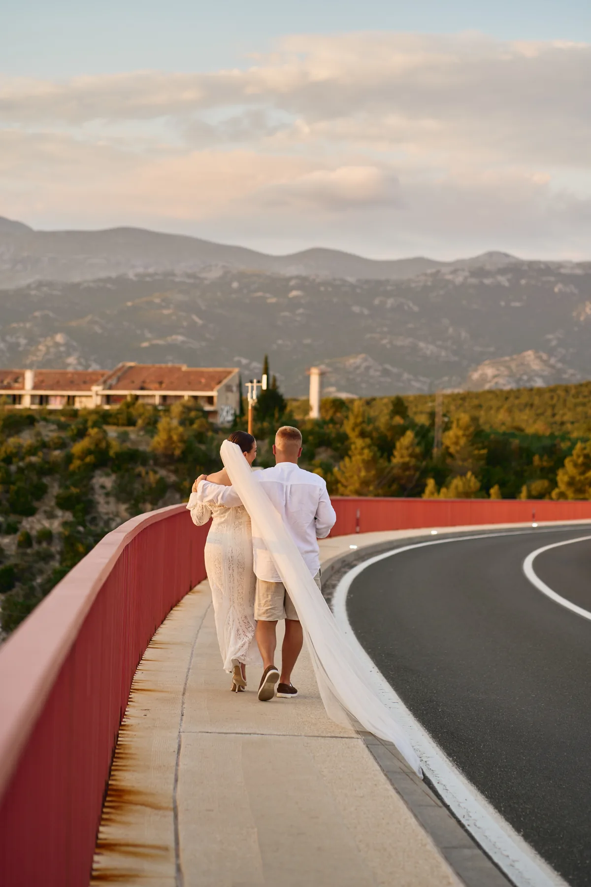 Newlyweds walking a bridge with the bride's veil flowing behind her