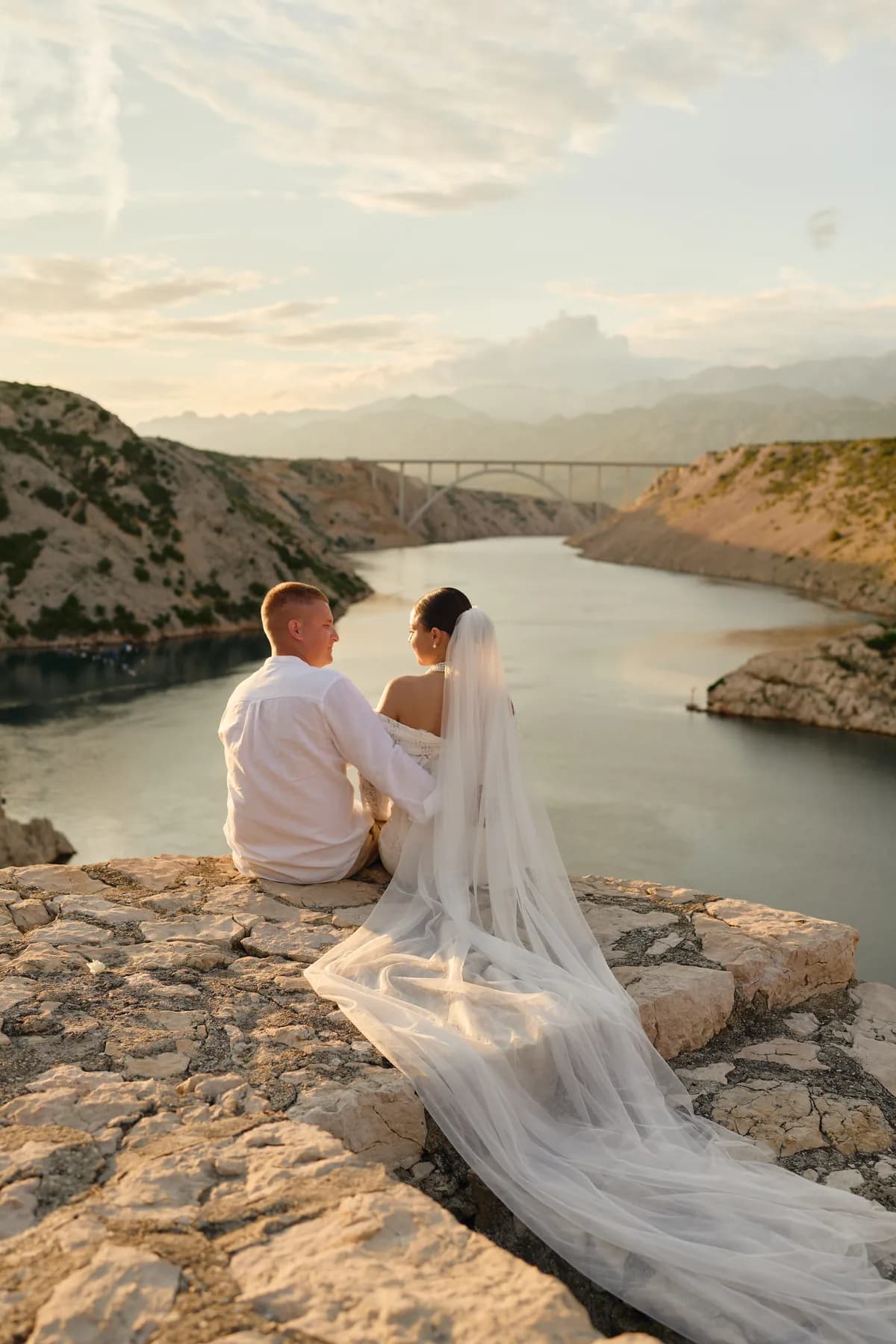 Bride and groom sitting above a river canyon with a long veil