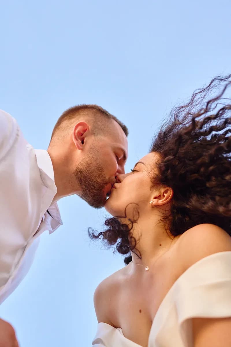 Newlyweds kissing against a clear blue sky