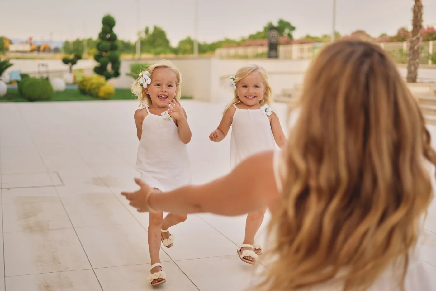 Two little girls in white dresses running to their mum, laughing, during a family photoshoot in Zadar