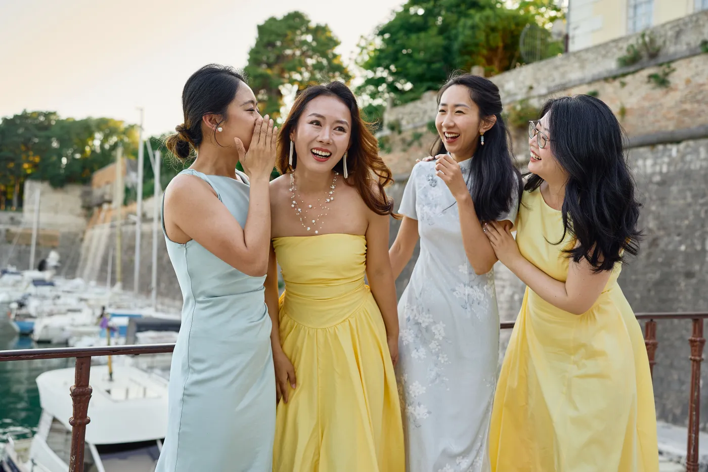 A group of friends in elegant dresses laughing together by the Zadar harbour during a photoshoot
