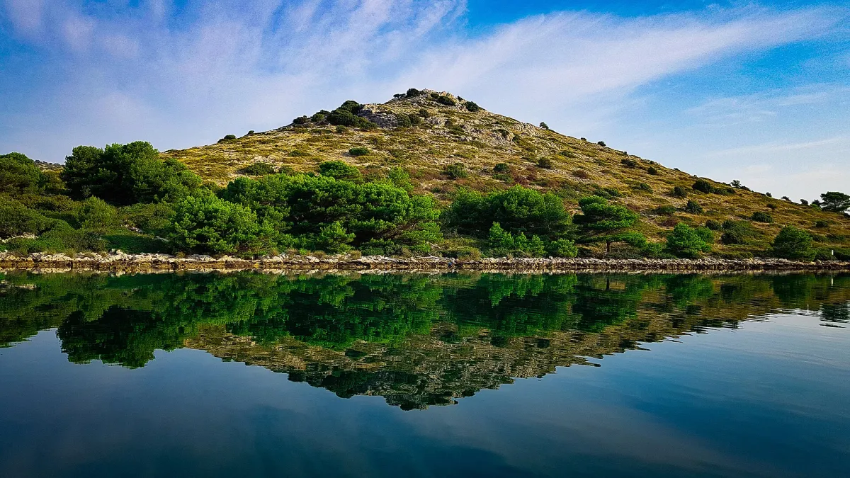 A green islet in the Kornati archipelago mirrored in still water